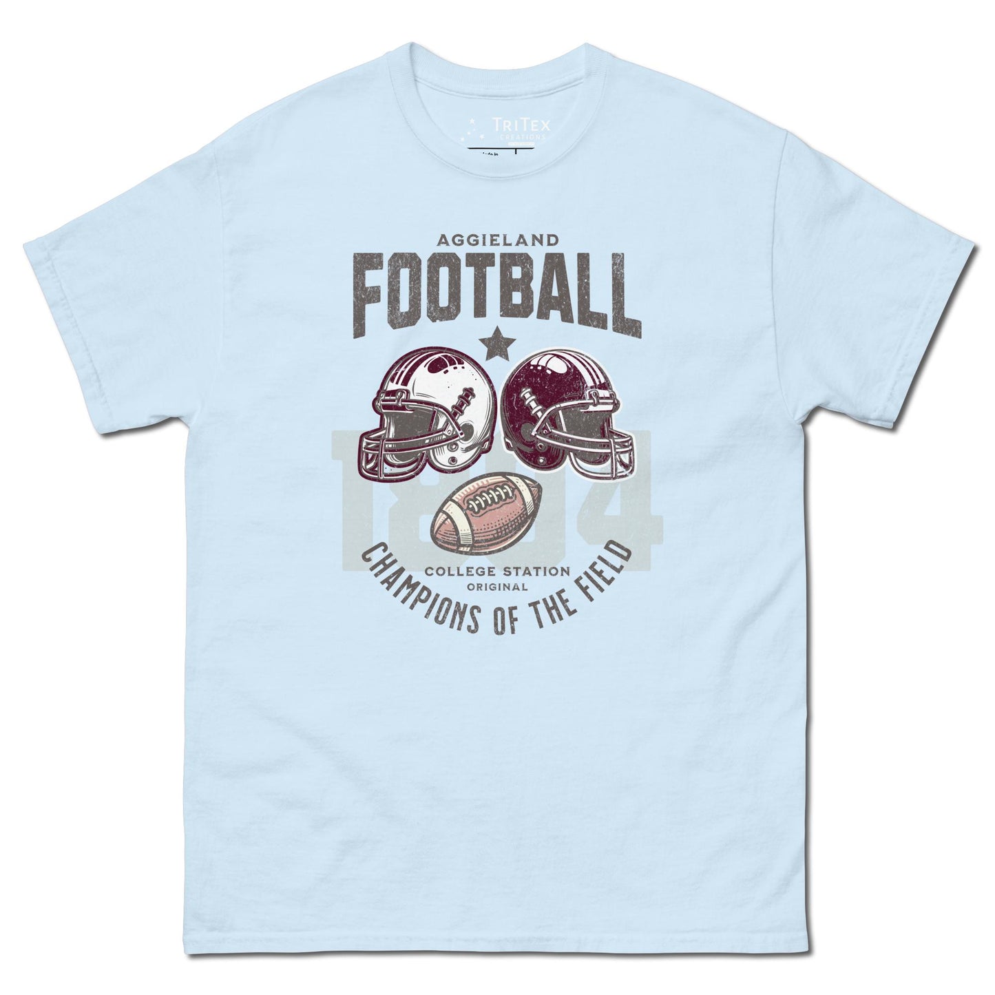 A light blue t-shirt featuring football helmets and a football with the text "Aggieland Football College Station original Champions of the field"