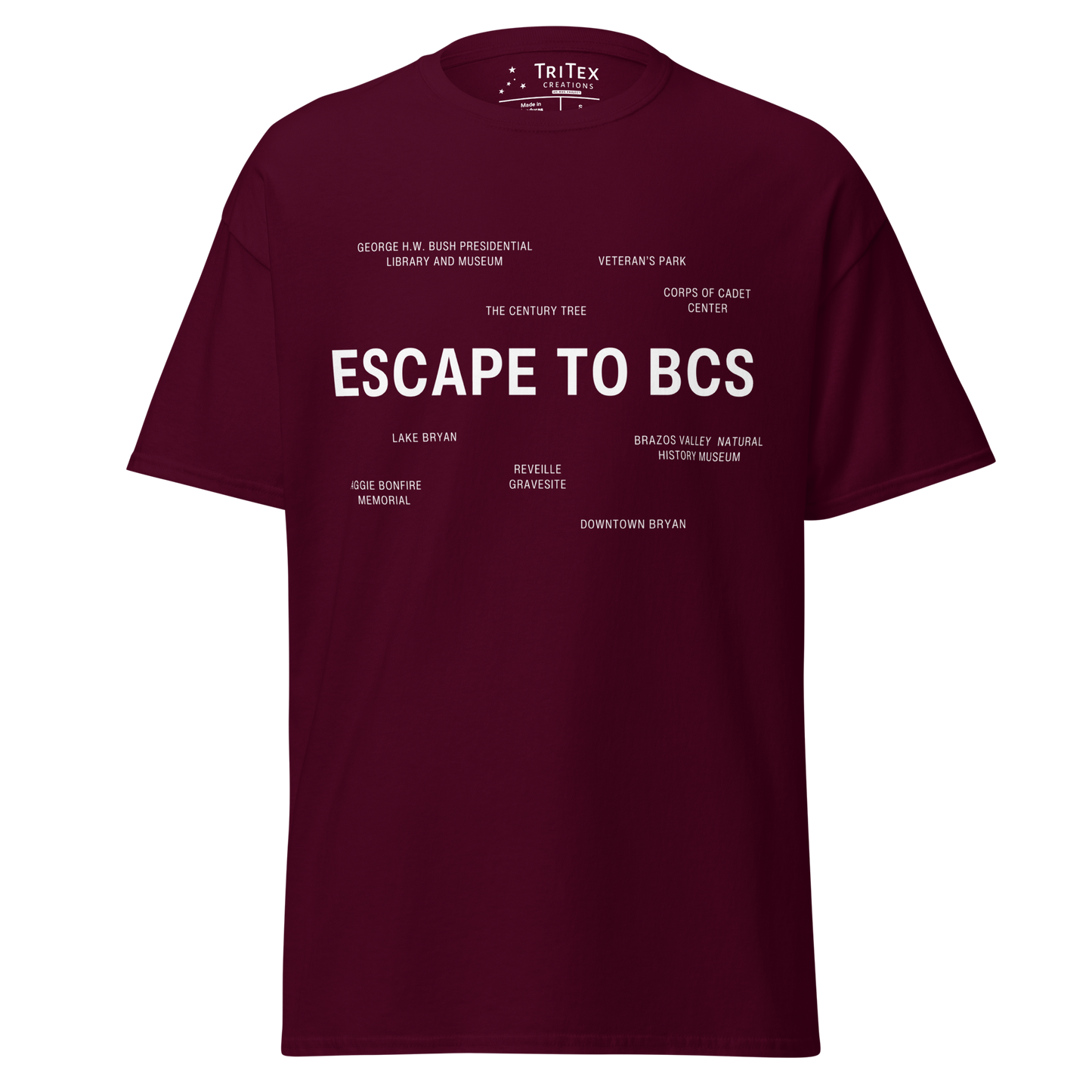 A maroon t-shirt which reads "Escape To BCS" in big, bold text with smaller text elements naming Bryan and College Station's landmarks.