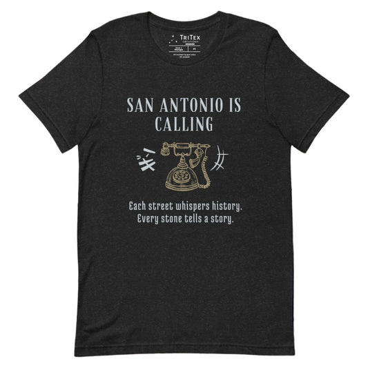 A black heather t-shirt featuring a graphic image of a vintage rotary phone with the text "San Antonio is calling. Each street whispers history. Every stone tells a story."