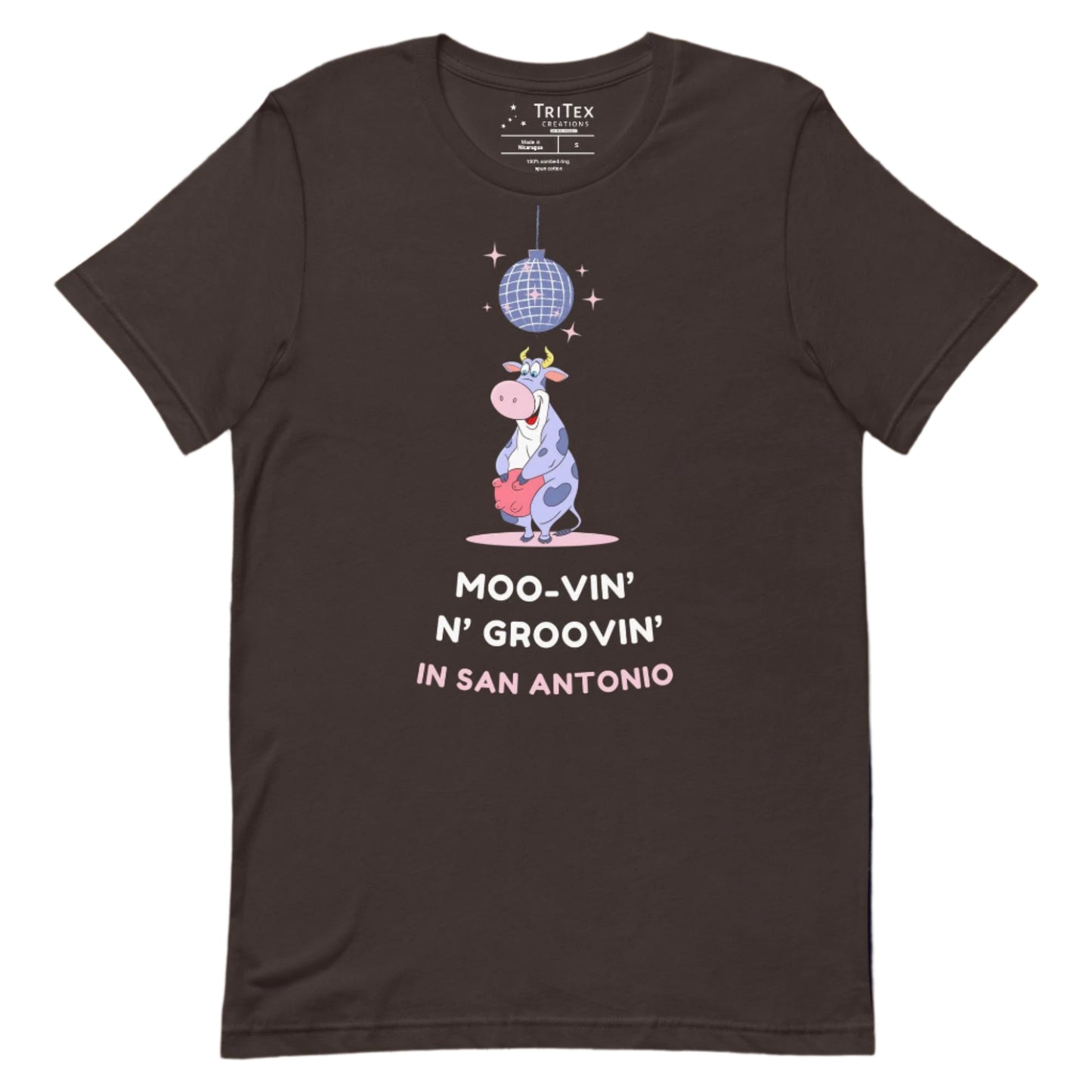 A brown t-shirt with a cartoon cow standing under a sparkling disco ball with the the text "Moo-vin' n' groovin' in San Antonio".