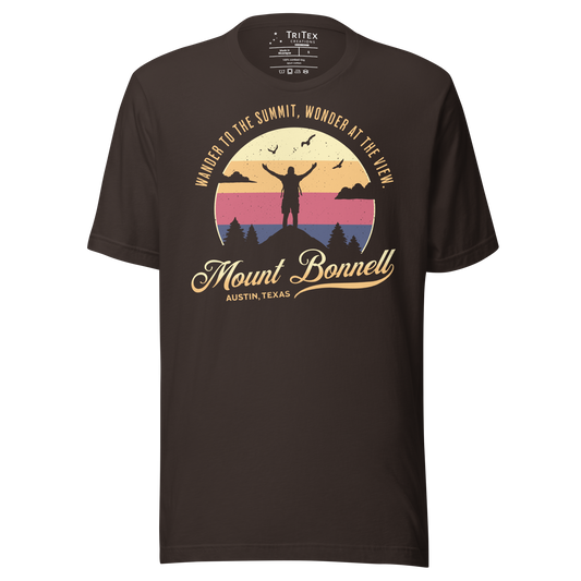 A brown t-shirt featuring the silhouette of a person standing on a mountain with the words "Wander to the summit, wonder at the view."