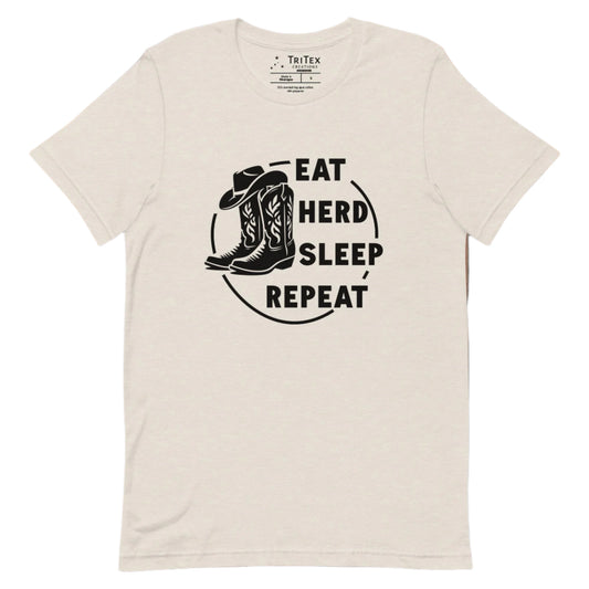 A heather dust t-shirt featuring boots and a cowboy hat with the words "Eat, herd, sleep, repeat".