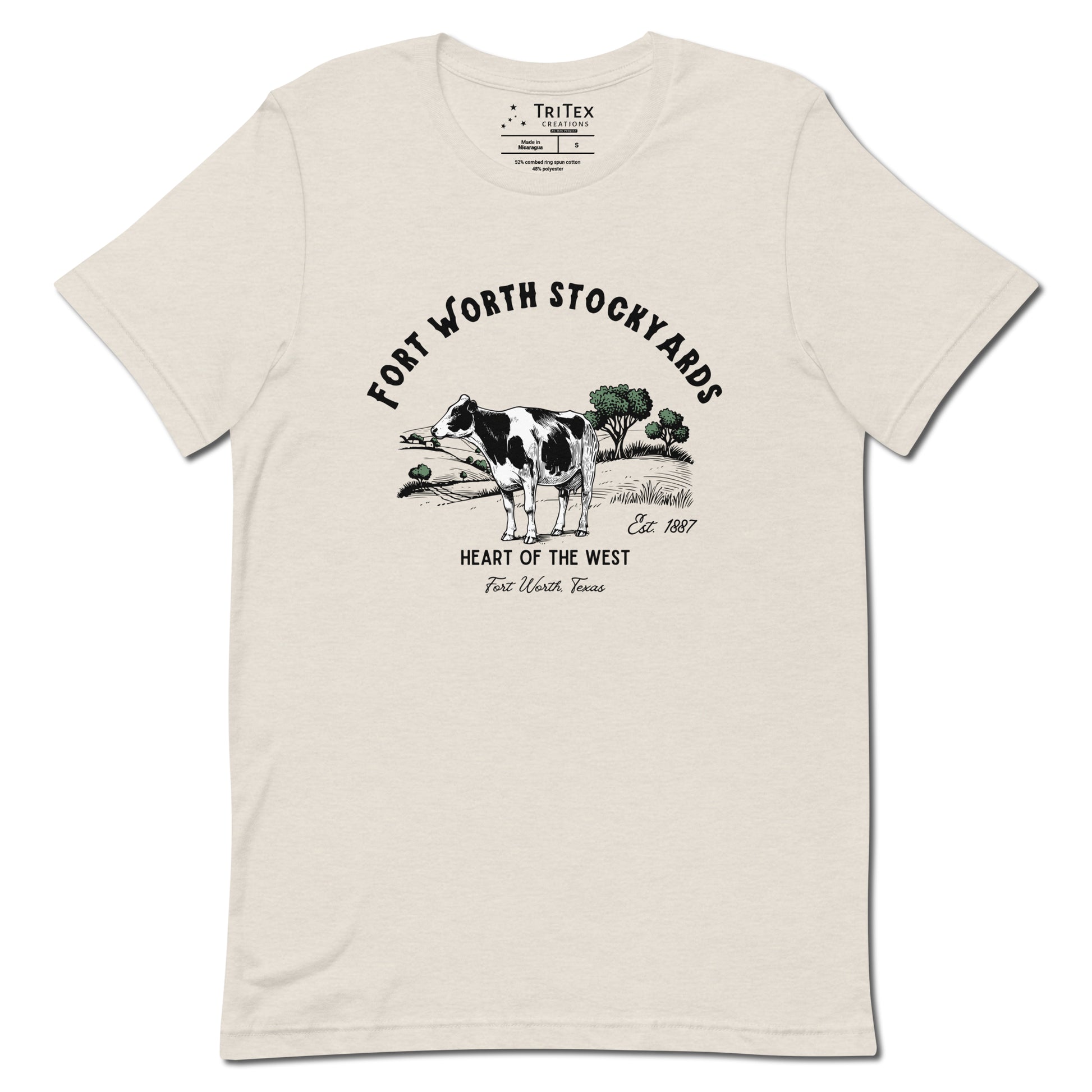 A heather dust t-shirt with a black and white jersey cow stands in a field with trees and text that reads "Fort Worth Stockyards Est. 1887 Heart of the West Fort Worth, Texas".