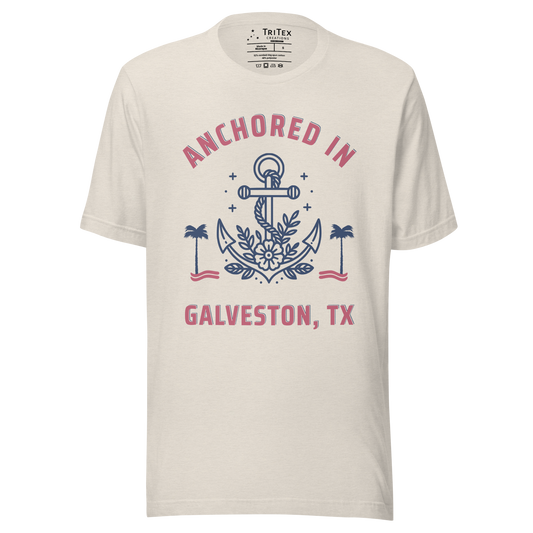 A heather dust t-shirt featuring an image of an anchor, palm trees and a flower with the text "Anchored in Galveston, TX".