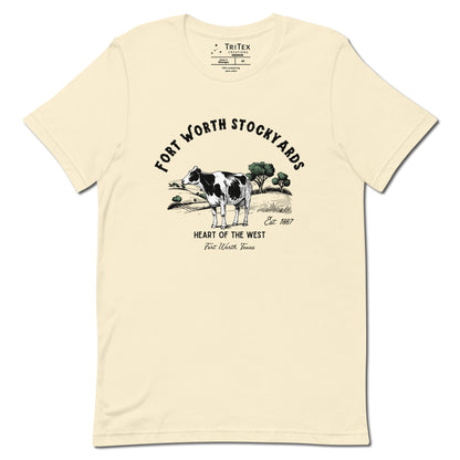 A natural-colored t-shirt with a black and white jersey cow stands in a field with trees and text that reads "Fort Worth Stockyards Est. 1887 Heart of the West Fort Worth, Texas".