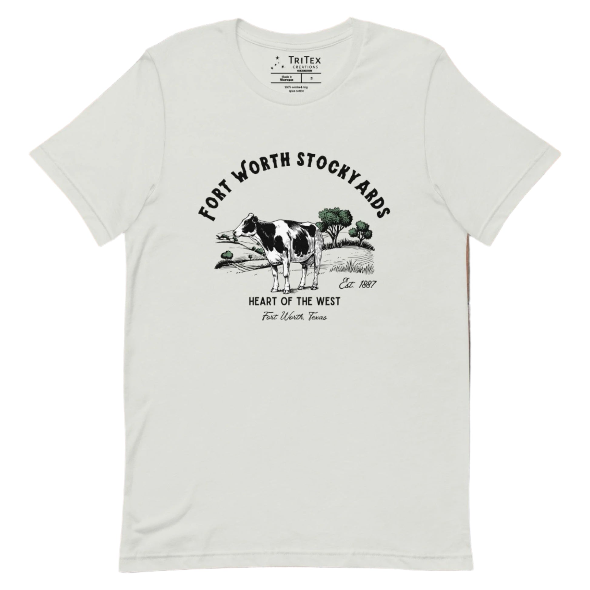 A silver t-shirt with a black and white jersey cow stands in a field with trees and text that reads "Fort Worth Stockyards Est. 1887 Heart of the West Fort Worth, Texas".