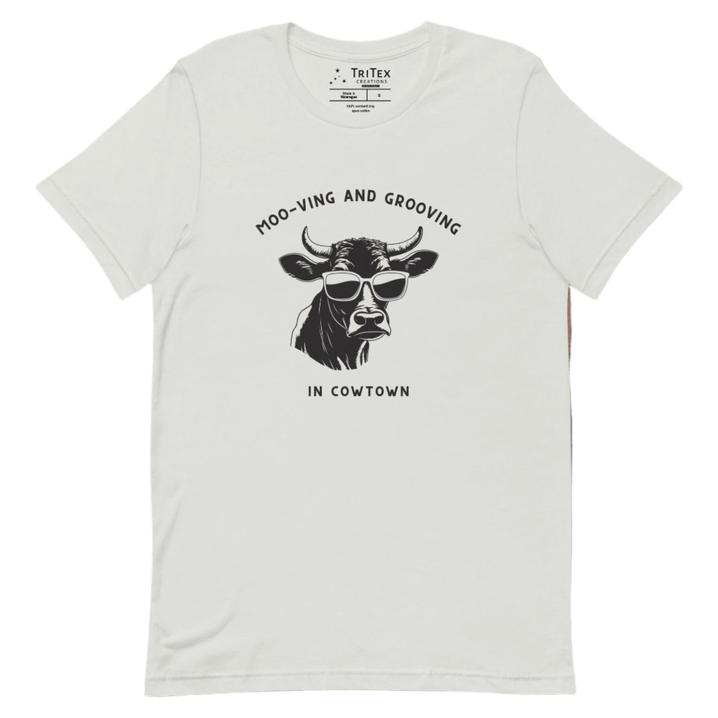 A silver t-shirt featuring an illustration of a cow wearing sunglasses with the the text "Moo-vin' n' groovin' in Cowtown".