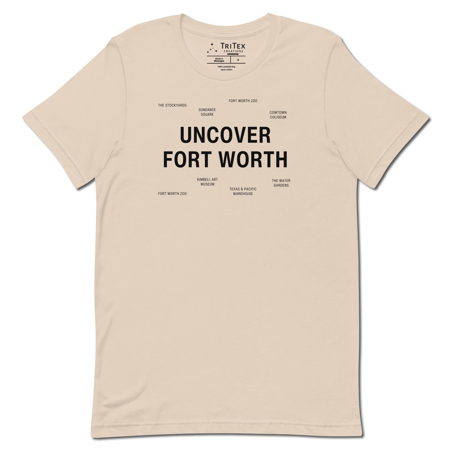 A soft cream t-shirt which reads "Uncover Fort Worth" in big, bold text with smaller text elements naming Fort Worth landmarks.