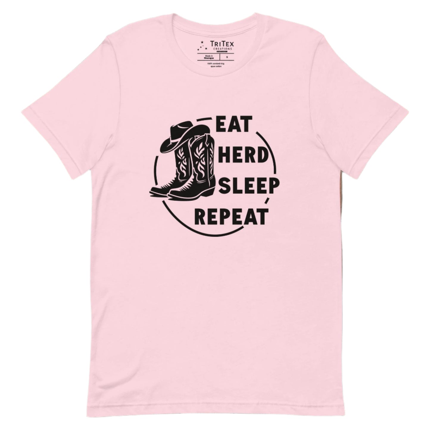 A soft pink t-shirt featuring boots and a cowboy hat with the words "Eat, herd, sleep, repeat".