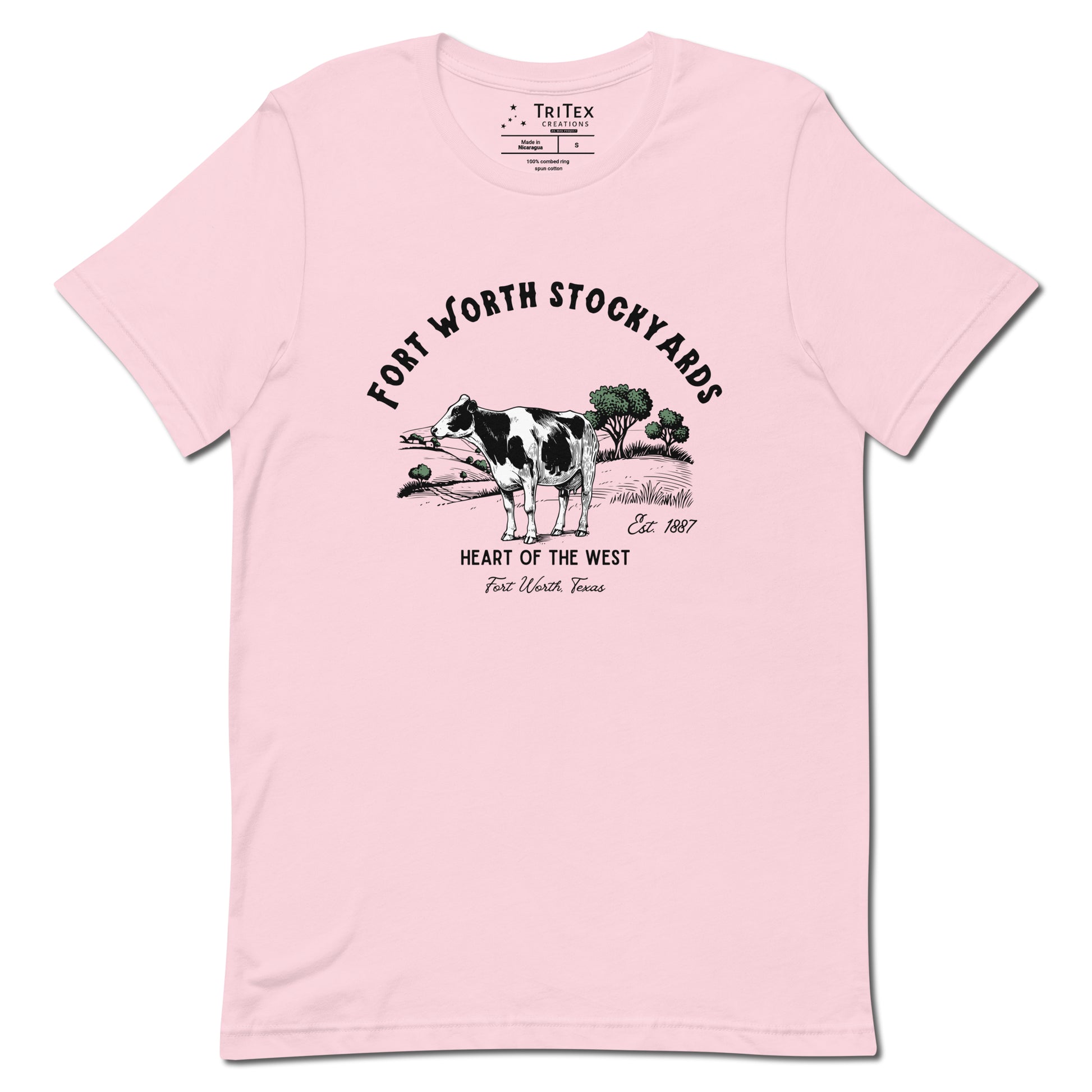 A soft pink t-shirt with a black and white jersey cow stands in a field with trees and text that reads "Fort Worth Stockyards Est. 1887 Heart of the West Fort Worth, Texas".