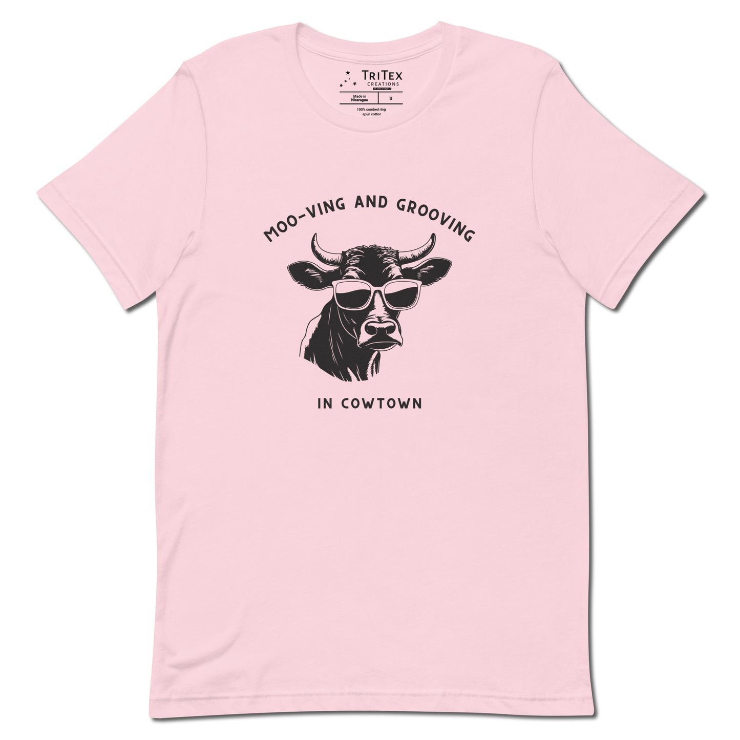 A soft pink t-shirt featuring an illustration of a cow wearing sunglasses with the the text "Moo-vin' n' groovin' in Cowtown".