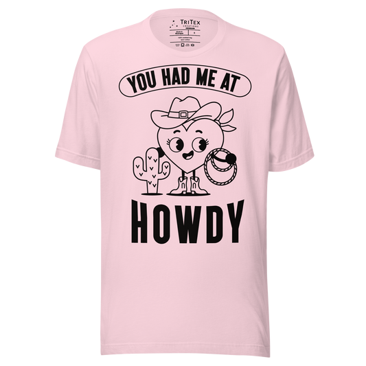 A soft pink t-shirt featuring a cartoon heart dressed like a cowboy with the words "You has me at howdy".