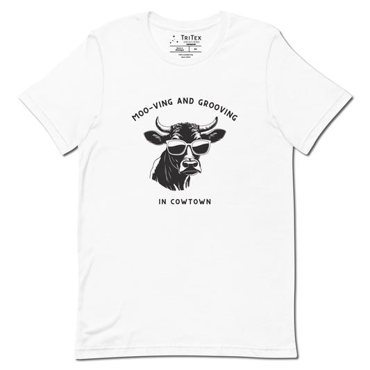 A white t-shirt featuring an illustration of a cow wearing sunglasses with the the text "Moo-vin' n' groovin' in Cowtown".